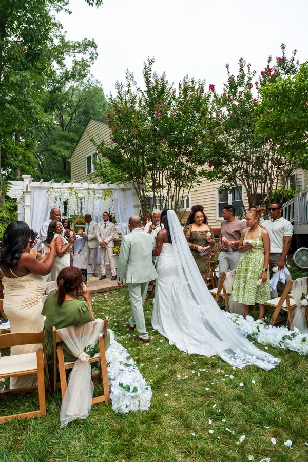 Bride and groom walk back down a petal-lined grass aisle as guests take photos