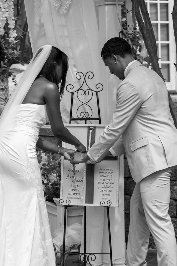 Black and white photo of a bride and groom braiding a cord of three strands during the ceremony