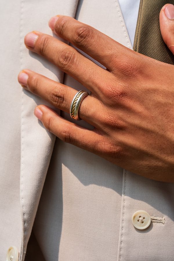 Close-up of a groom's hand on his cream suit lapel showing a two-tone wedding band